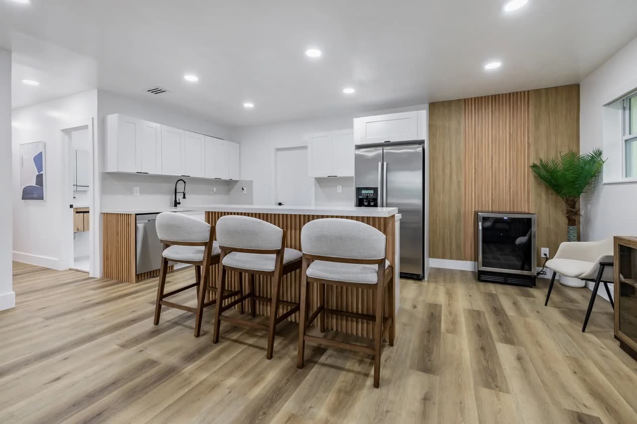 After the remodel: white cabinets, a fluted wood island with bar seating, recessed lighting and wood-look floors