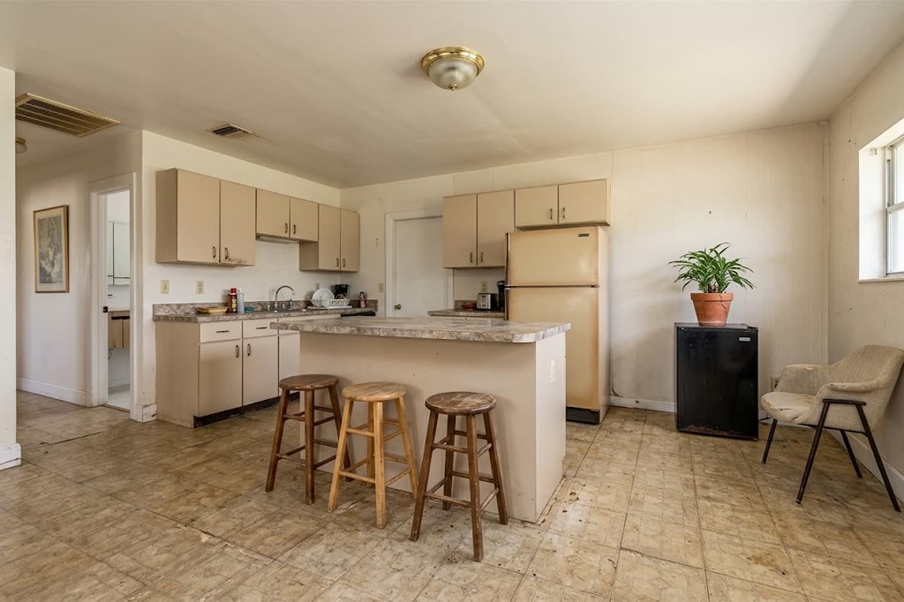Before the remodel: beige cabinets, a laminate peninsula with stools and worn tile floors